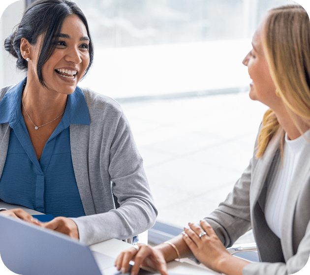 Two women engaged in a friendly meeting, sharing smiles and conversation.