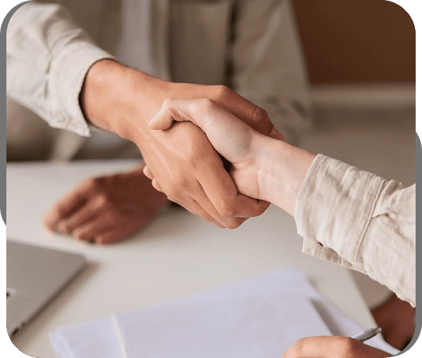 Two people shaking hands over a desk with documents.