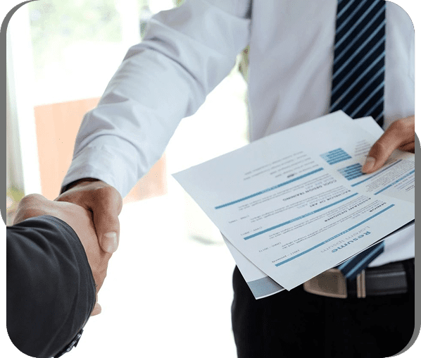 Two professionals shaking hands during a job interview with resumes in hand.