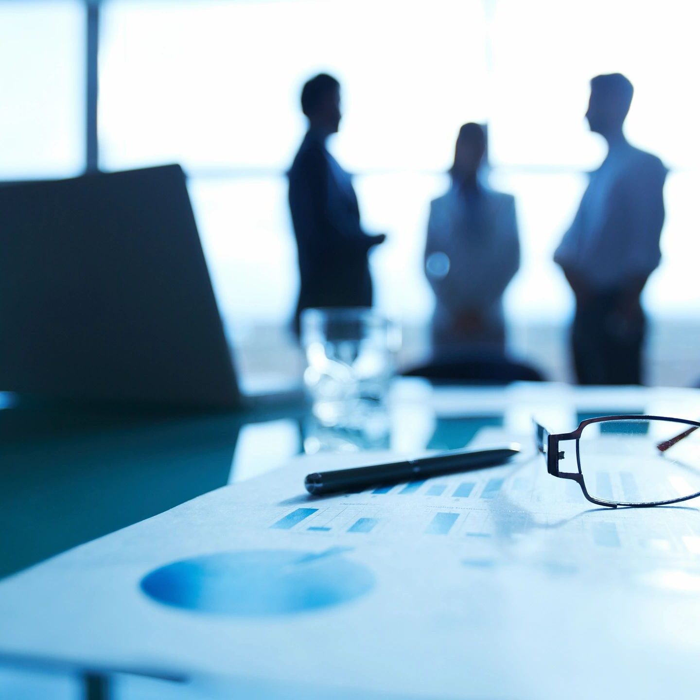 Close-up of documents with silhouettes of people in a meeting room.